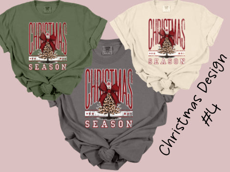 Three Christmas-themed t-shirts in green, gray, and beige on a pink background.